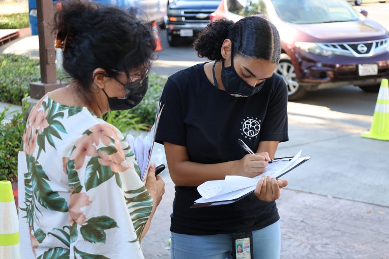 two volunteers with masks on and one person is writing on a clipboard