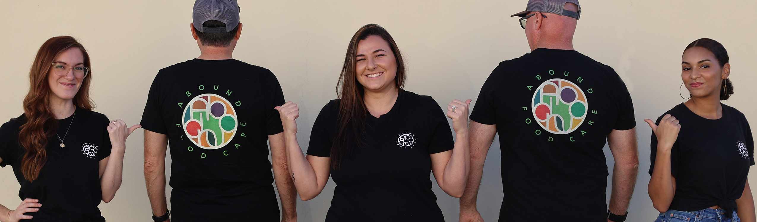 Abound Food Care team with people pointing to their logo on the back of other people's shirts